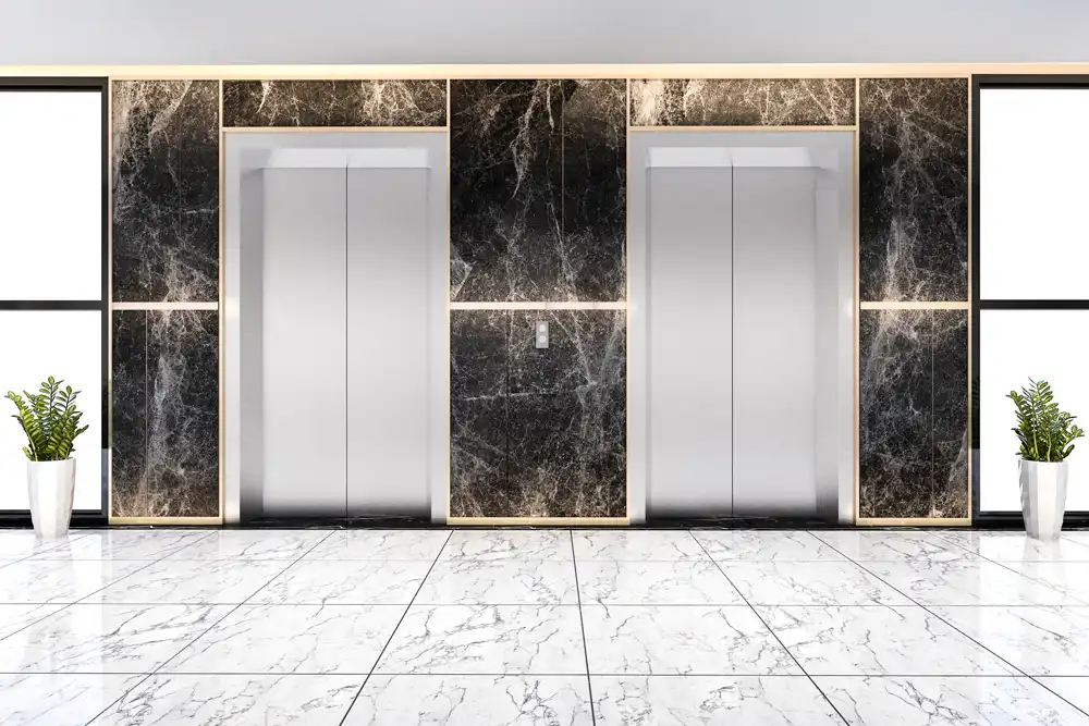 چند آسانسور با درب آلومینیومی و نمای سنگی در کنار هم در کنار دو گلدان سفید با گل طبیعی