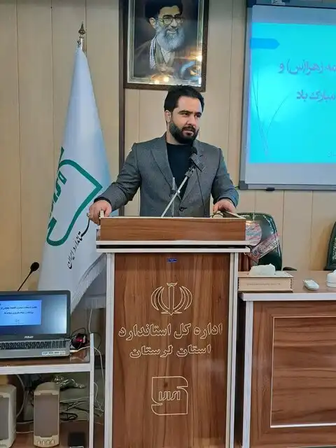 مدیرکل استاندارد لرستان در حال سخنرانی پشت یک میز چوبی